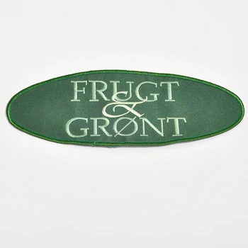 Aflang oval broderet patch med lys tekst på grøn baggrund